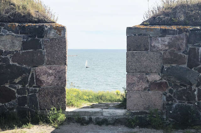 Turvekattoisten graniittimuurien välistä näkyy aurinkoinen ulappa ja siellä yksi purjevene