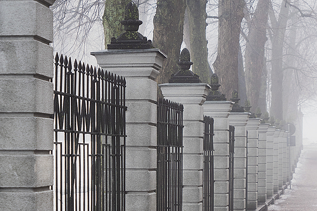 Sumuinen näkymä Venäjän Helsingin-suurlähetystön kivestä ja takoraudasta valmistetusta portista. Taustalla suuria, lehdettömiä puita.