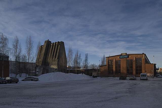 Talvisessa kuvassa korkea, erikoisen muotoinen betonirakennus ja tiilinen halli