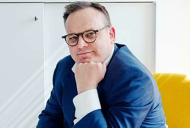 Silmälasipäinen mies katsoo kameraan