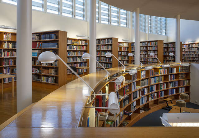 A curved interior space with strip windows above wooden bookselves