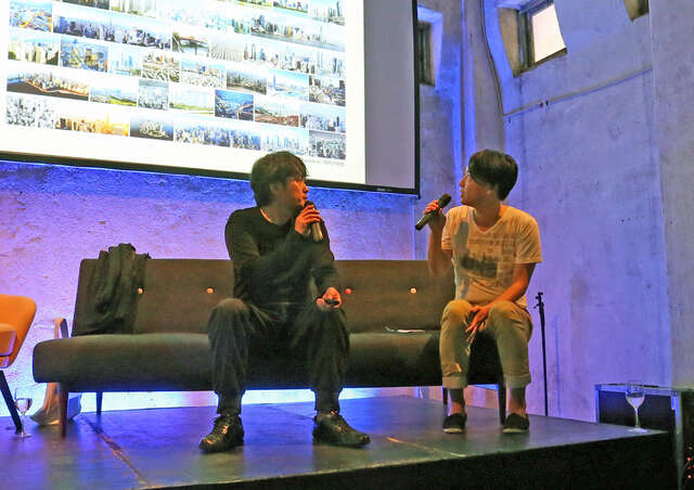 Two people on stage talking to each other with microphones in hand