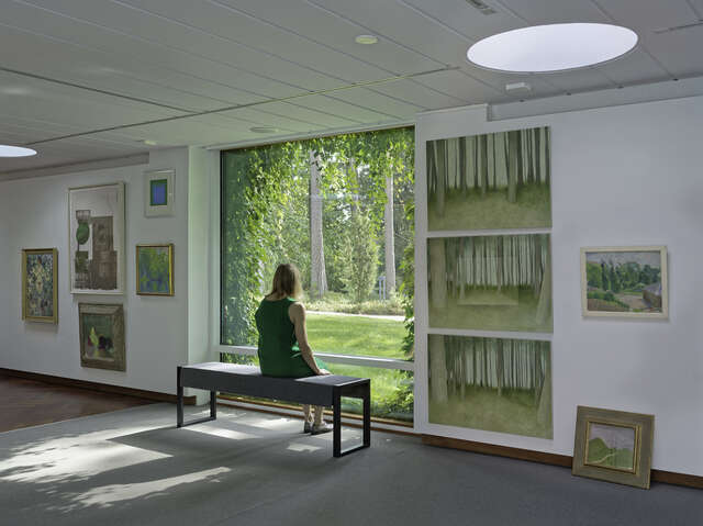 A woman in a green dress looks out of the window onto a green courtyard