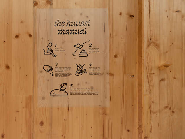 Puuseinälle liimattu tarra, jossa lukee The huussi manual ja sen alla kaaviomaisia piirroksia