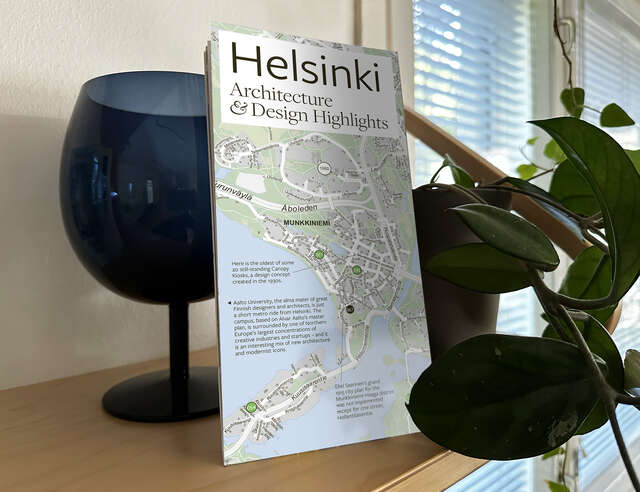 Kuva asetelmasta, jossa on taustalla lasiesine ja sen edessä kartta. Oikeassa reunassa näkyy osa viherkasvista.