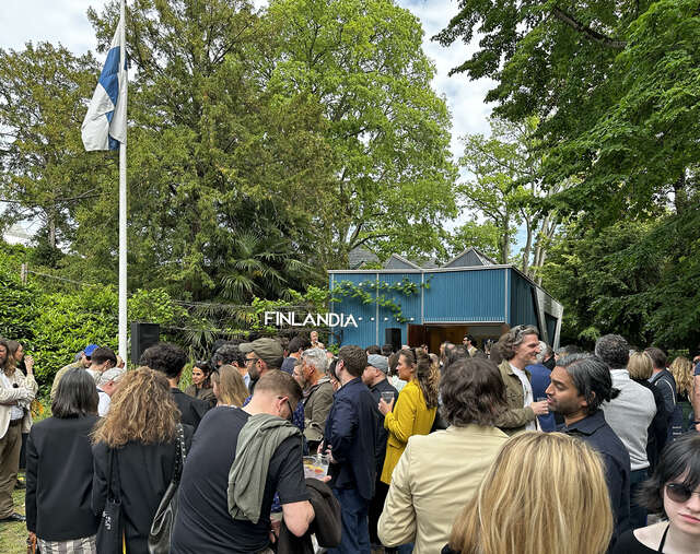 A crowd in front of a small blue pavilion. Finnish flag hoisted.
