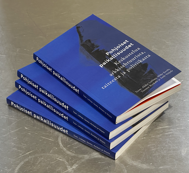 Neljä sinimustaa kirjaa pinossa metallialustalla