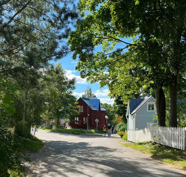 Punainen ja vaalea omakotitalo tien päässä. Tietä reunustavat lehtevät puut.
