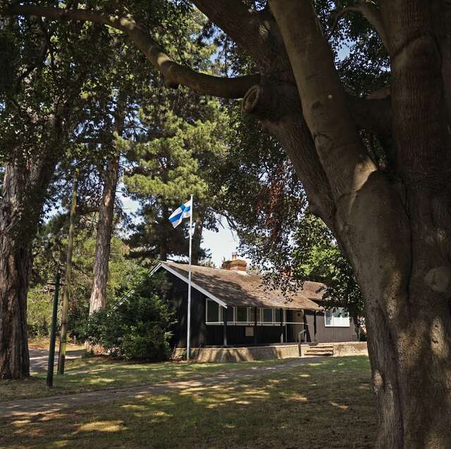 Puurakenteinen saunarakennus metsässä, lipputangossa Suomen lippu.