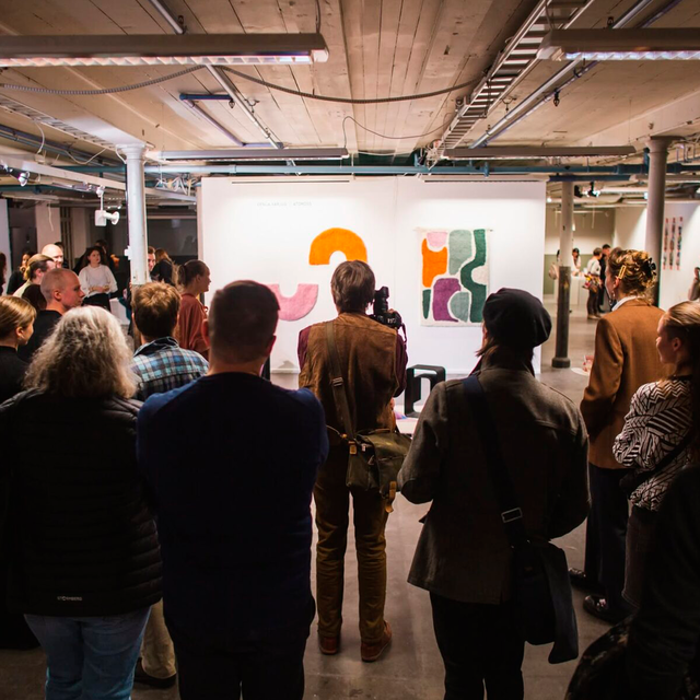 A group of people are viewing colourful artwork on a screen with their backs to the viewer.