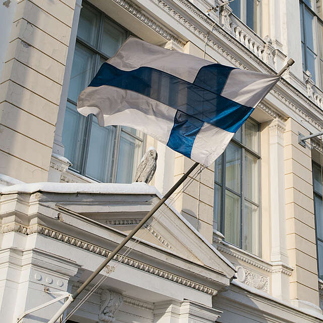 A white flag with a blue cross hoisted on the facade of a classical building.