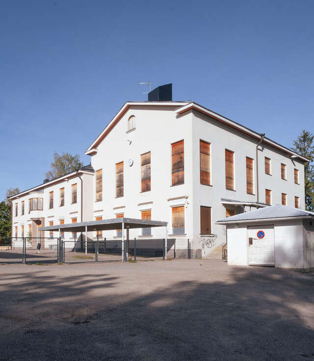 An old vacant primary school whit white facades and windows covered in plywood