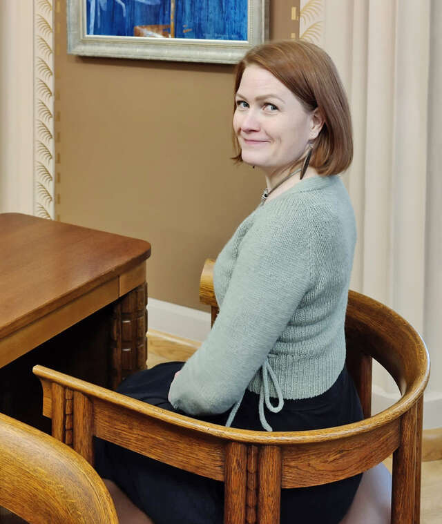 Hymyilevä nainen istumassa poseeraten kameralle.