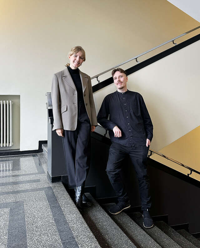 A woman and a man in stairs, leaning against the handrail.