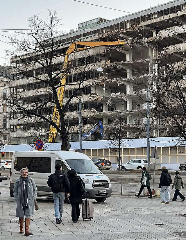 A crane demolishing a city block, people watching