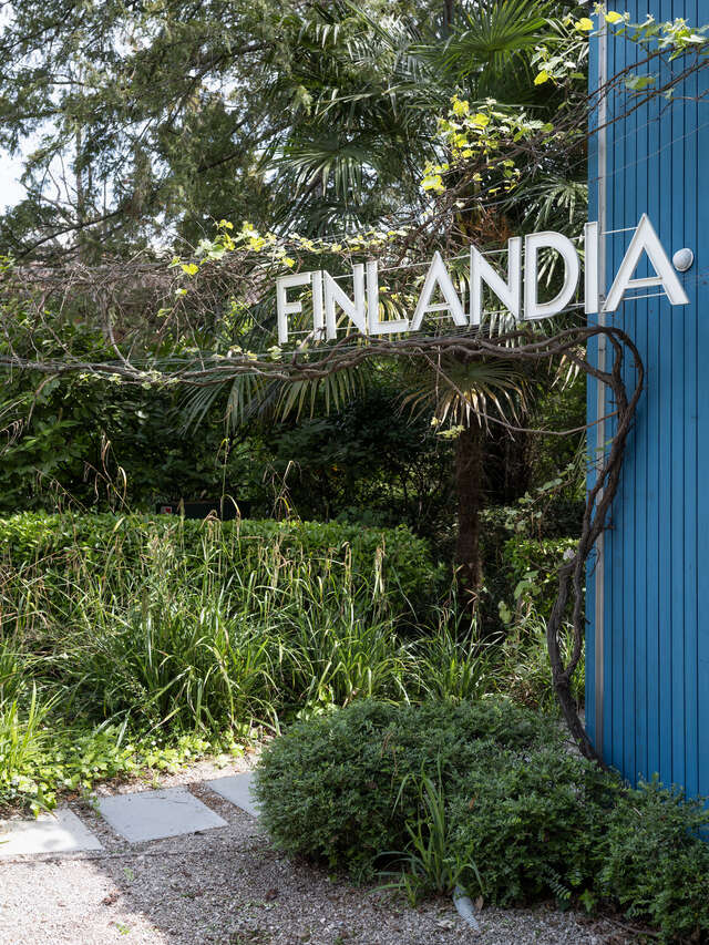 White Finlandia-lettering outside a blue wooden pavilion.