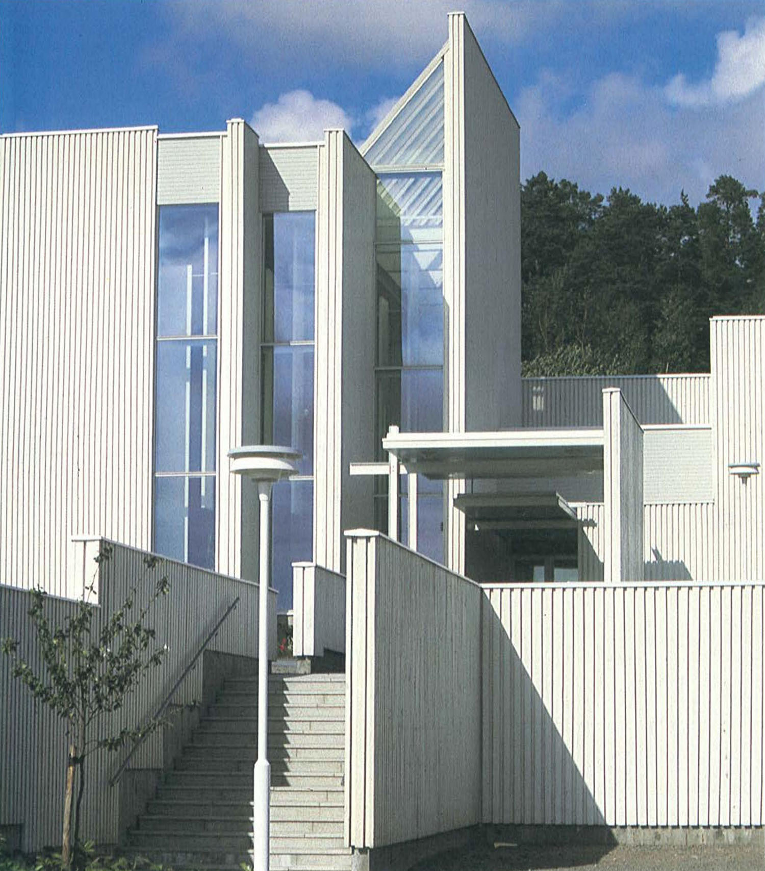 Lähikuva valkoiseksi maalatusta puurakennuksesta, jossa pystyseinämien väliin jää korkeita kapeita lasiosia