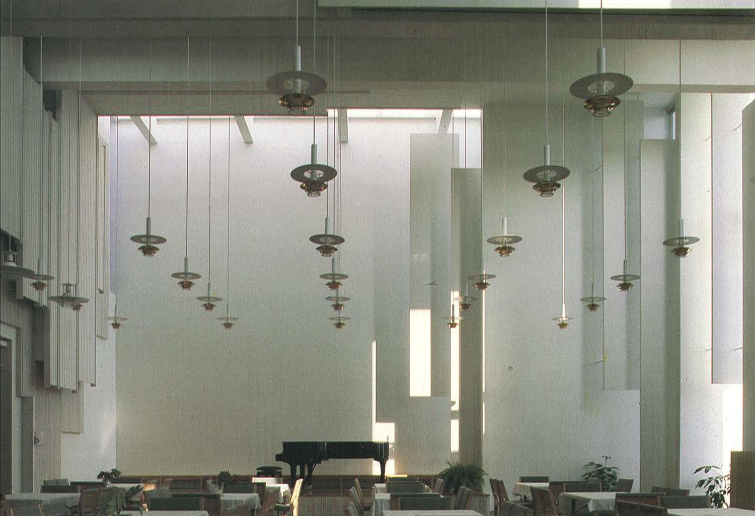 Korkea, vaalea sisätila, johon tulee epäsuoraa valoa ja jossa roikkuu useita valaisimia