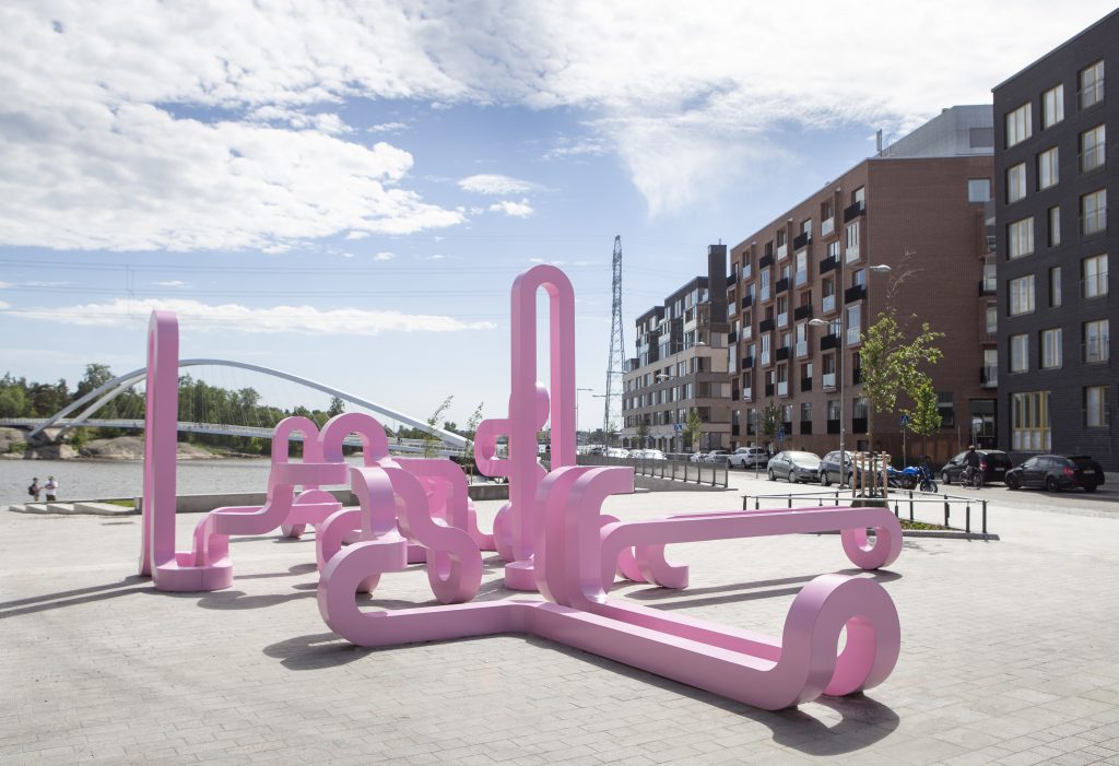 Kalasataman Capellanaukiolla sijaitseva vaaleanpunainen kiermurteleva veistos, joka on kuinA pink meandering sculpture at Capellanaukio Square in Kalasatama, the sculpture is like one continuous line that never ends. yhtä jatkuvaa viivaa, joka ei pääty koskaan.