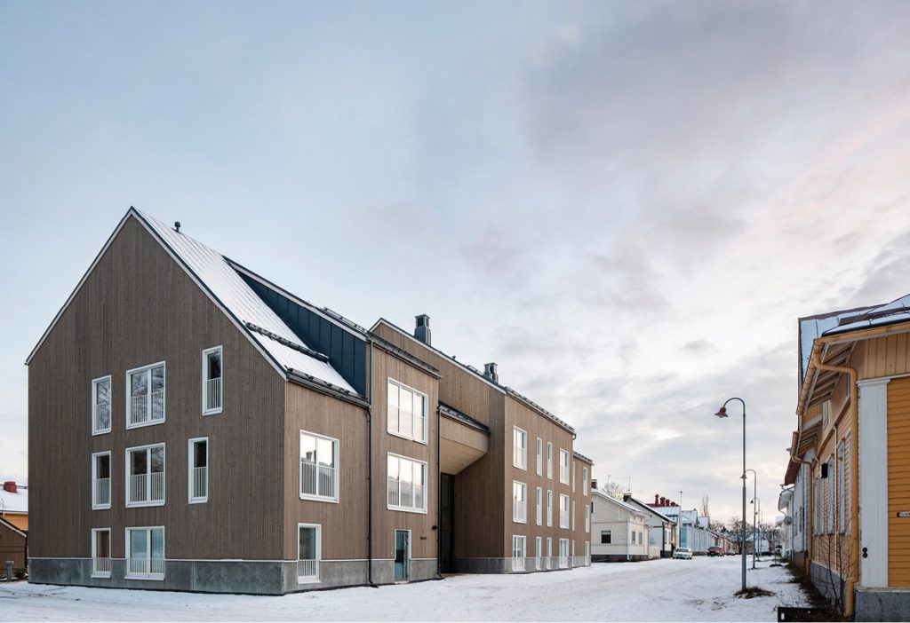 A pitched-roof three-storey wooden house in a street aligned by low buildings