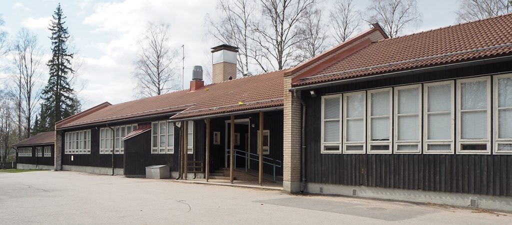 Facade with dark, vertical planks, entrance canopy in the middle.