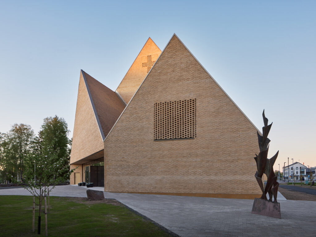 Three triangular, yellow brick volumes, cross made in the brick surface on top