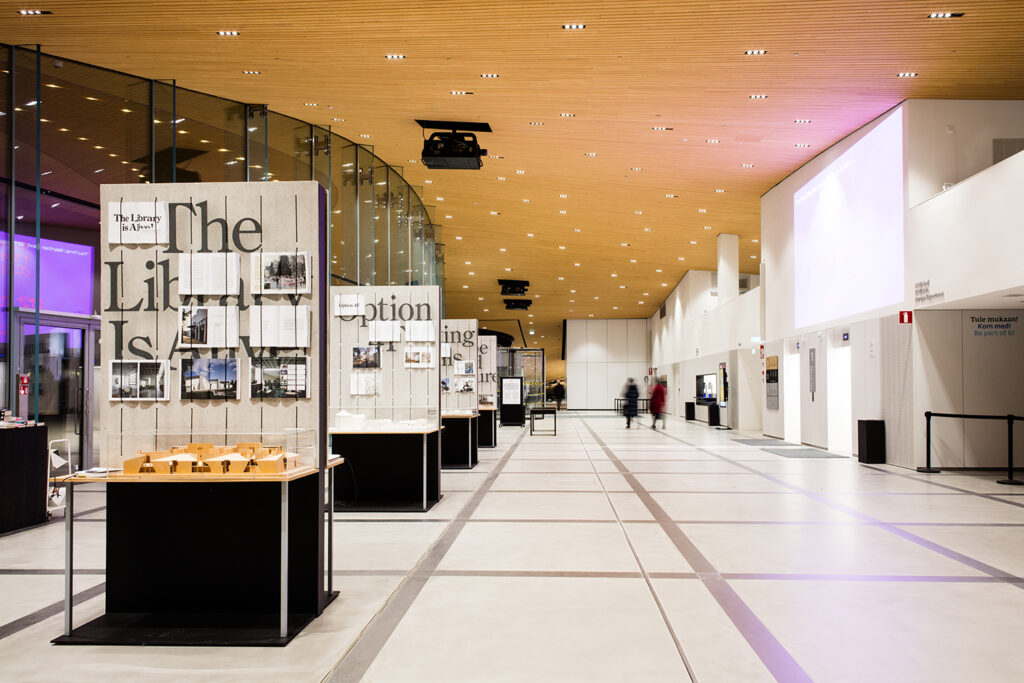 A hall with a curved wooden roof. On the left side there are exhibition walls with books hung on them and scale models.