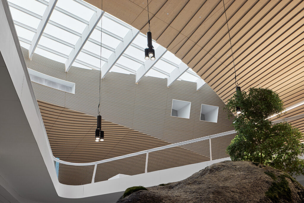 A photo from inside a big building. A wood cladded ceiling and a big skylight can be seen through an opening between two floors.