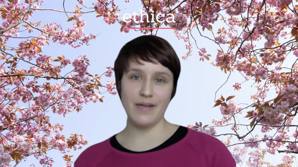 Pinkkiin paitaan pukeutunut nainen puhuu kameralle, taustakuvana kirsikankukkia ja teksti Ethica.